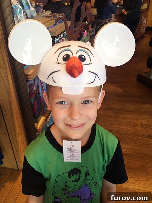 A little boy wearing an adorable Olaf hat with Mickey ears, smiling brightly.