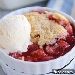 A close-up of a rustic strawberry cobbler with golden-brown biscuit topping, hinting at its delicious warmth and sweetness.