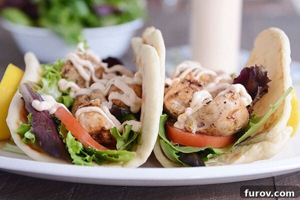 Two vibrant grilled lemon chicken wraps, generously filled with tender chicken, fresh vegetables, and a creamy, spicy garlic sauce.