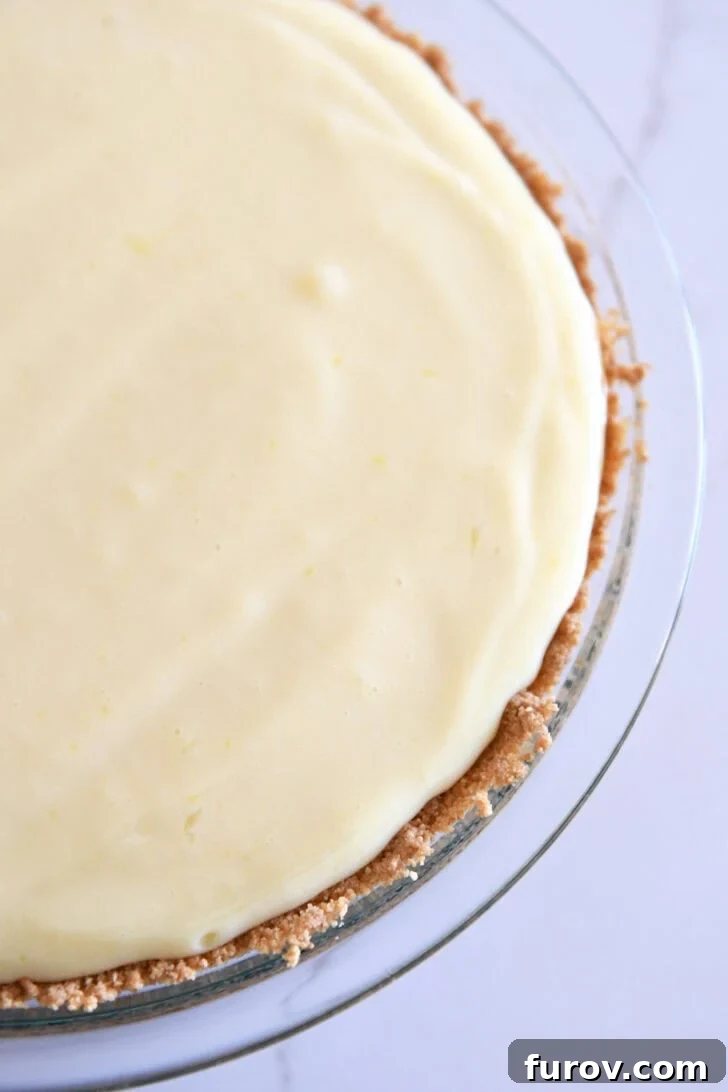 Top down view showing half of a lemon pie with a graham cracker crust in a glass pie dish.