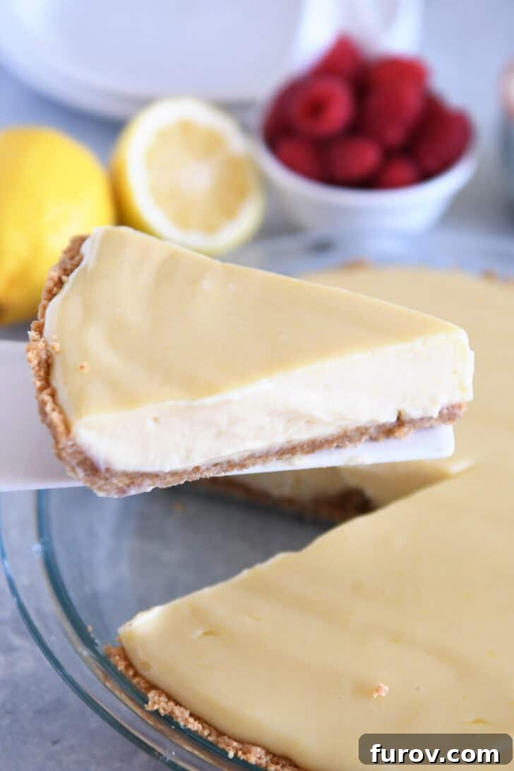 A spatula taking a slice of graham-cracker crust lemon pie out of a full lemon pie.
