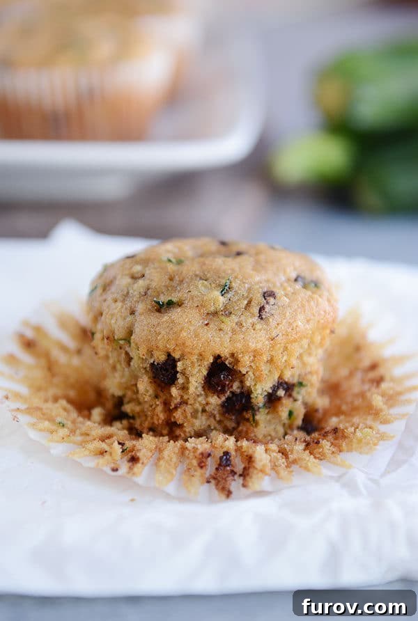 A chocolate chip zucchini muffin, cut in half to show its moist interior and generous chocolate chips, sits on a napkin, ready to be enjoyed.