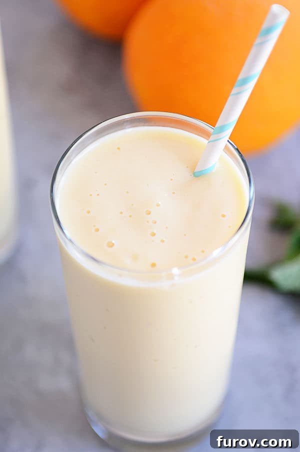 Tall glass cup of vibrant orange dreamsicle smoothie with a straw, evoking a refreshing summer vibe and ready to be enjoyed.