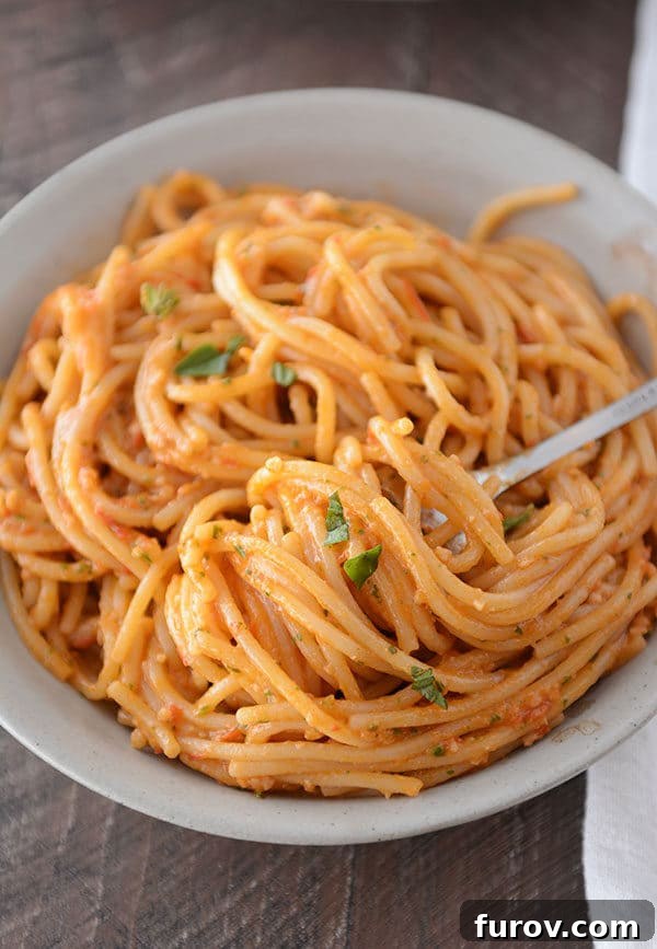 A fork getting a large bite of tomato pesto spaghetti noodles on it from a white bowl of pasta.