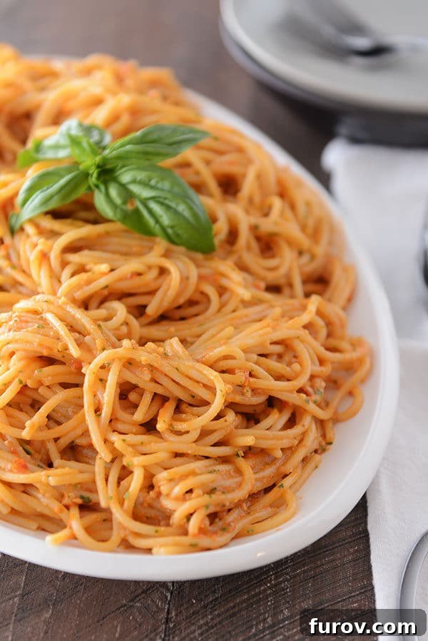 A large oval white bowl full of cooked tomato pesto pasta.