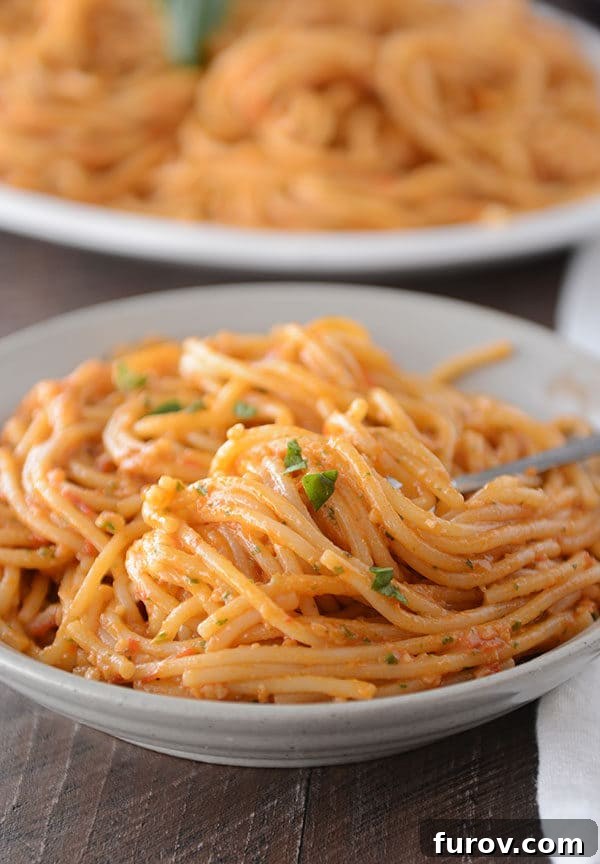 A white bowl of tomato and pesto coated spaghetti noodles.
