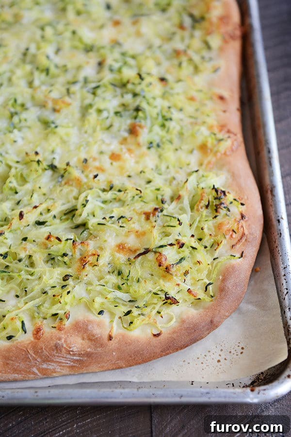 A golden-baked zucchini and cheese-topped pizza, fresh from the oven, viewed from above on a baking sheet.