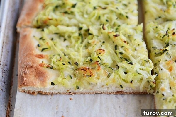 A freshly baked zucchini and cheese-topped pizza, sliced into generous portions, resting on a baking sheet.
