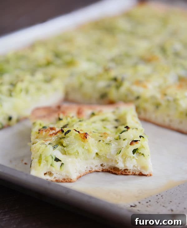 A baking sheet featuring a zucchini and cheese pizza, with several slices already removed, and one slice having a bite taken out.