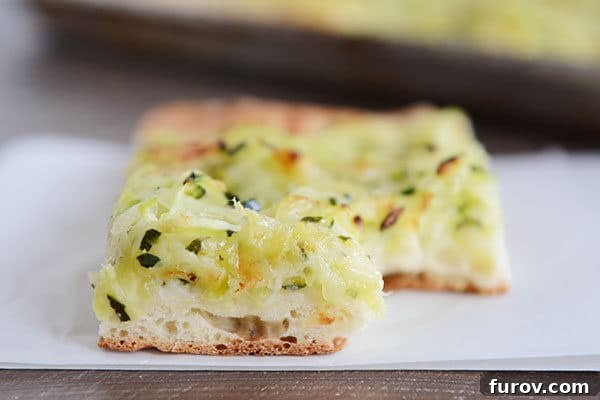 A delicious slice of cheesy zucchini pizza with a bite taken out, showing the golden crust and melted topping.