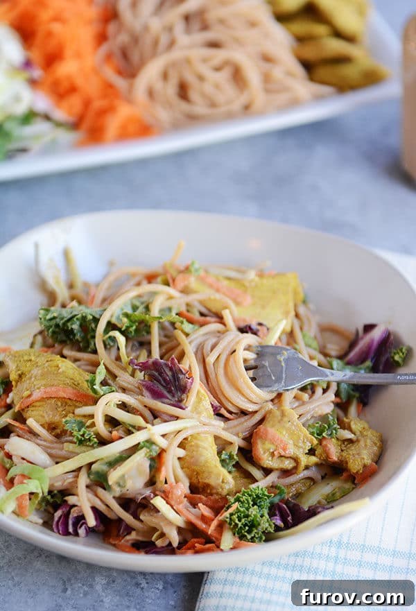 Thai Peanut Chicken Noodle Salad 2 A fork taking a bite of noodles out of a bowl of chicken noodle salad, showcasing vibrant colors and textures.