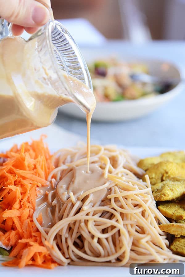 Thai Peanut Chicken Noodle Salad 3 Creamy satay dressing being poured generously over a bed of freshly cooked noodles.