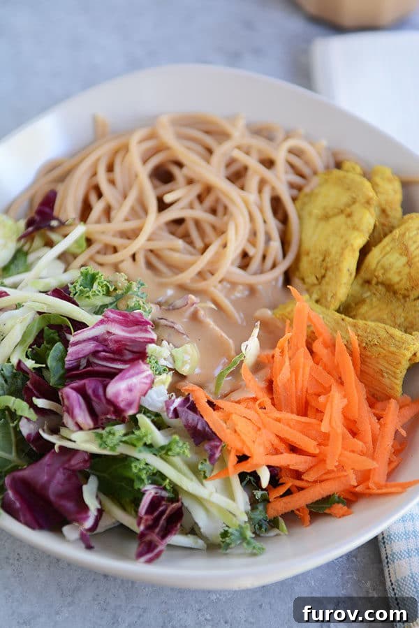 Thai Peanut Chicken Noodle Salad 4 A beautifully presented white bowl of satay chicken noodle salad, featuring shredded carrots, chicken, noodles, and dressing.