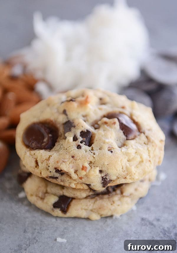 Two chocolate chunk, almond, coconut cookies stacked on top of each other.