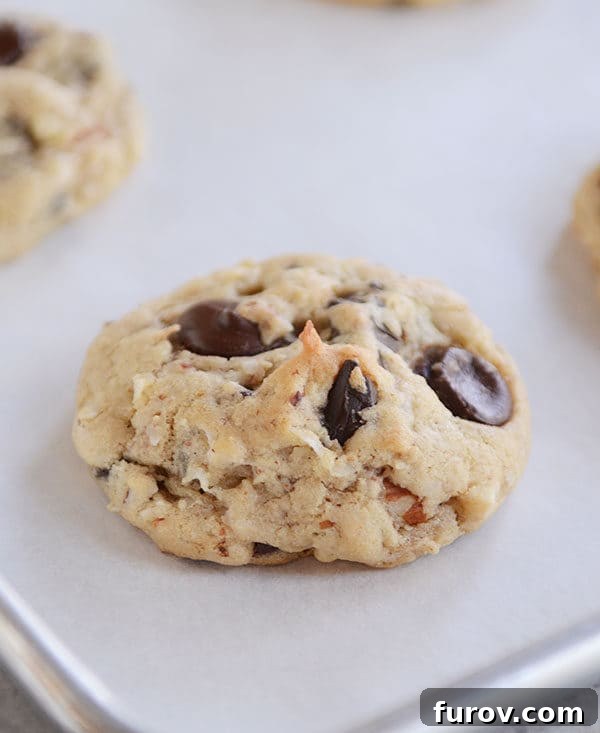 A cookie with large chocolate chunks and coconut on a cookie sheet.
