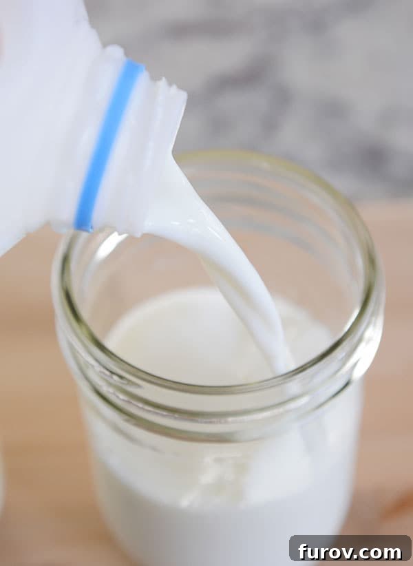 A stream of fresh milk being poured into a mason jar containing milk kefir grains, starting the fermentation process.