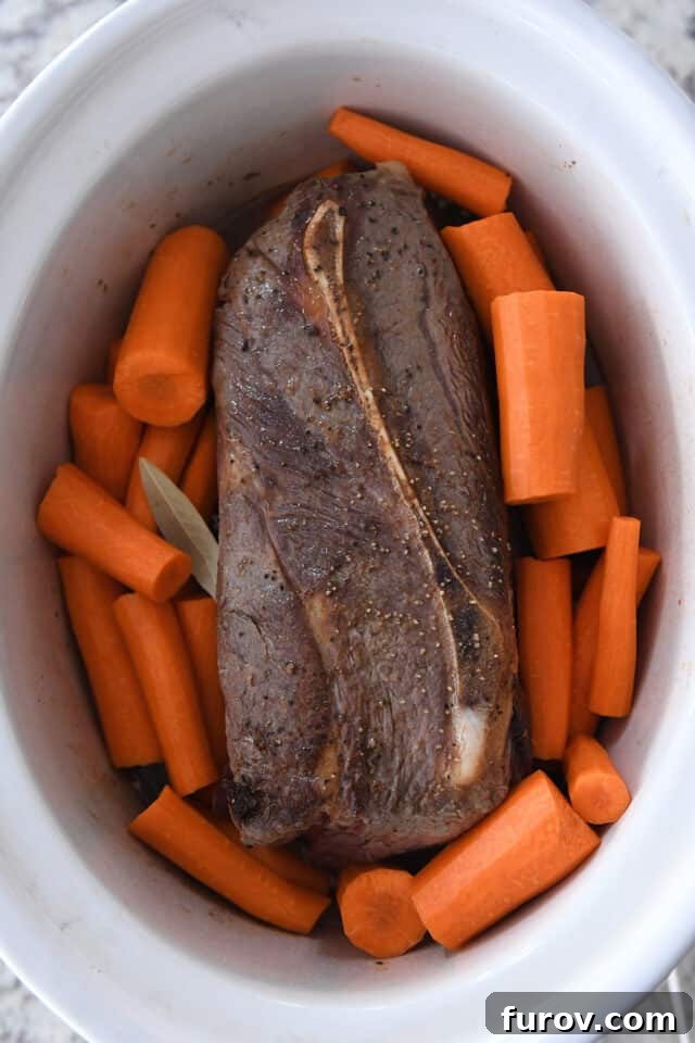 Melt-in-Your-Mouth Pot Roast and Savory Gravy 3 Slow cooker insert with a browned pot roast, large carrot pieces, and a bay leaf simmering in a rich broth.