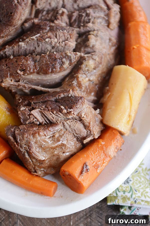 Melt-in-Your-Mouth Pot Roast and Savory Gravy 5 Top view of a pot roast sliced up with cooked carrots and potatoes around it, showcasing its tender texture.