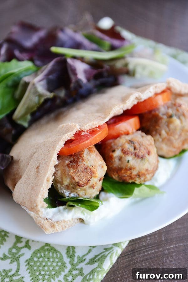 Juicy Greek Meatball Stuffed Pitas with Creamy Tzatziki 2 A meatball and veggie stuffed Greek pita next to a large serving of lettuce on a white plate.