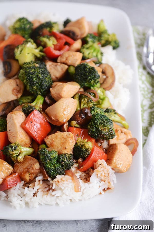 Top view of a white platter of cooked white rice topped with chicken and vegetables.