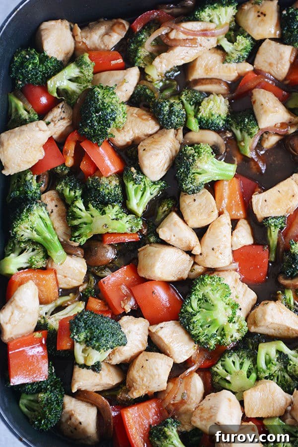 Top view of a skillet of cooked chicken, broccoli, peppers, and onions.