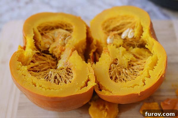 Quick and Easy Pressure Cooker Pumpkin Puree 6 A cooked pumpkin cut neatly in half on a wooden cutting board, revealing the soft, bright orange flesh and easily removable seeds.