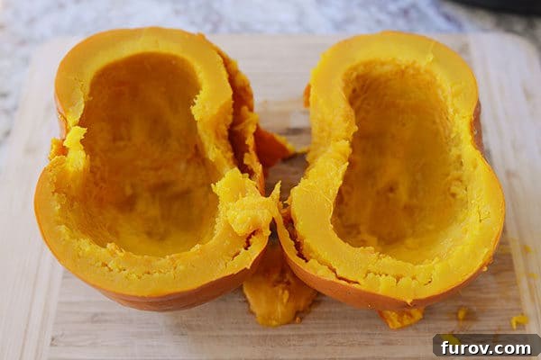 Quick and Easy Pressure Cooker Pumpkin Puree 8 One half of a cooked pumpkin, with the skin visibly curling away from the bright orange flesh, resting on a wooden cutting board.