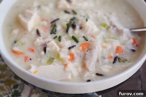 A white bowl of creamy chicken and wild rice soup with a spoon resting on the side, ready to be enjoyed.