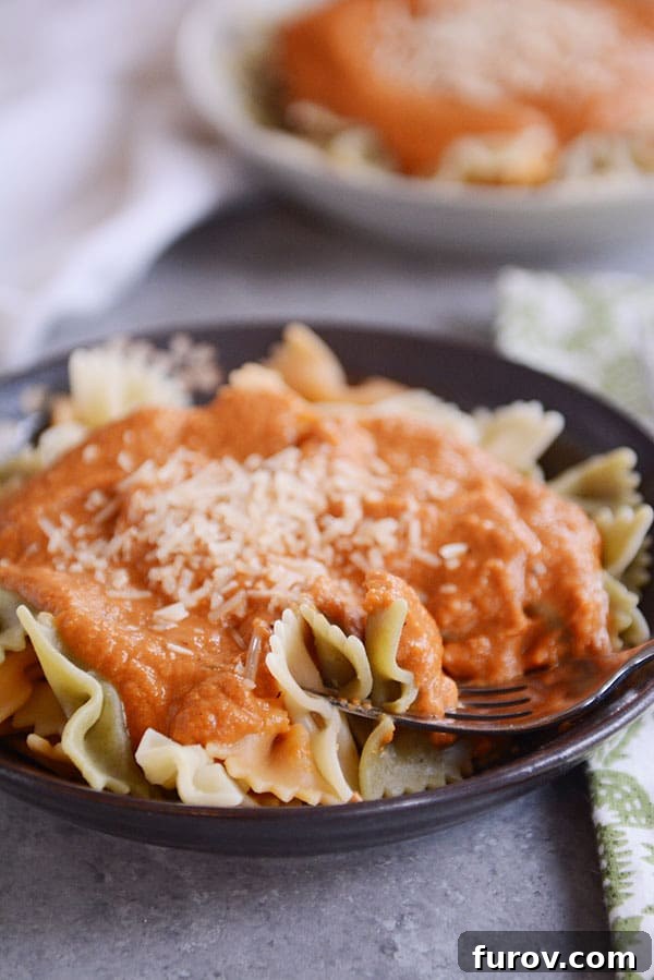 A close-up view of a dark bowl filled with perfectly cooked bowtie pasta, richly coated in the creamy, autumn-hued Trader Joe's copycat harvest pasta sauce, topped with grated Parmesan.