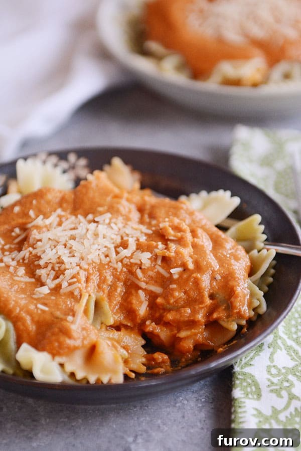 Another enticing shot of cooked bowtie pasta generously covered in homemade Trader Joe's copycat harvest pasta sauce, sprinkled with grated Parmesan cheese in a dark bowl.