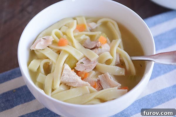Effortless Flavorful Chicken Noodle Soup 4 A white bowl of chicken noodle soup with a spoon in the side.