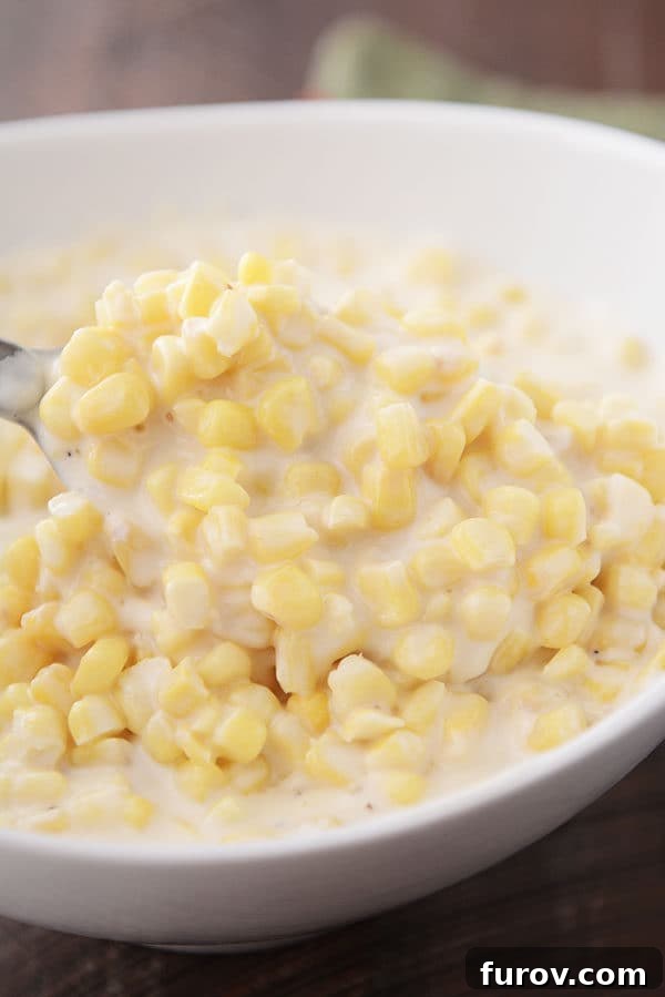 Velvet Parmesan Corn 2 A spoon taking a large scoop of creamy parmesan cream corn out of a white oval bowl, highlighting its rich texture.