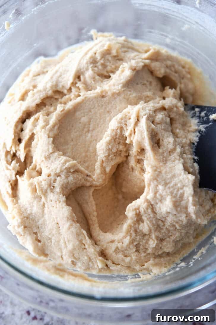 A top-down view of the smooth, golden-brown cookie batter in a clear glass bowl after all the base ingredients and softened butter have been thoroughly combined, showcasing its rich and uniform texture.