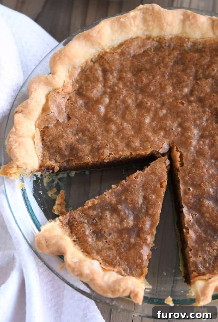 A top-down view of a perfectly baked chocolate chip cookie pie with a clean slice already removed, revealing its golden crust and molten, chocolate-filled interior, ready for serving.
