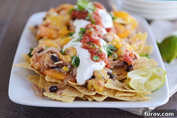 A close-up top-down view of a white platter featuring irresistible cheesy fajita nachos, generously topped with cool sour cream and fresh salsa.