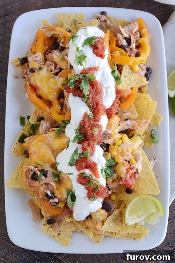 An inviting top view of a white platter brimming with cheesy fajita nachos, artfully garnished with sour cream and fresh salsa.