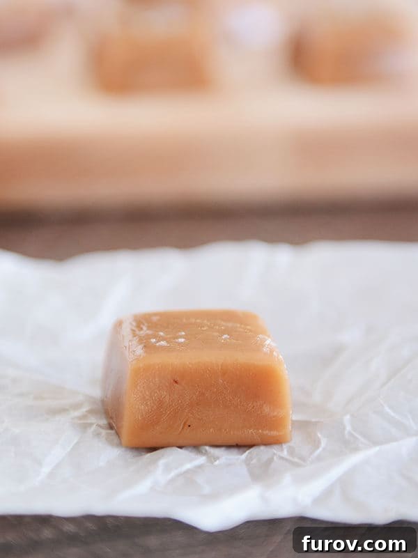 Perfect Vanilla Bean Caramels A Step-by-Step Guide 2 An unwrapped salted vanilla bean caramel on a piece of parchment, showcasing its rich, golden hue and smooth texture.