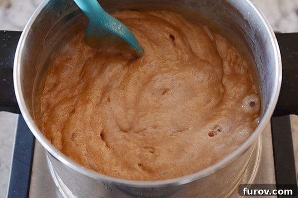 Perfect Vanilla Bean Caramels A Step-by-Step Guide 5 A pot of bubbling caramel being stirred with a plastic spoon, showcasing the rich, amber color.