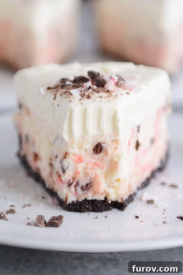 Front view of a slice of white chocolate peppermint cheesecake with a small bite taken out, revealing its rich interior.