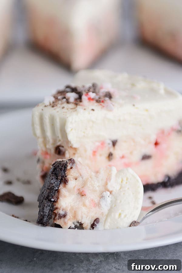 A fork taking a bite out of a slice of layered peppermint white chocolate cheesecake, highlighting its creamy texture.
