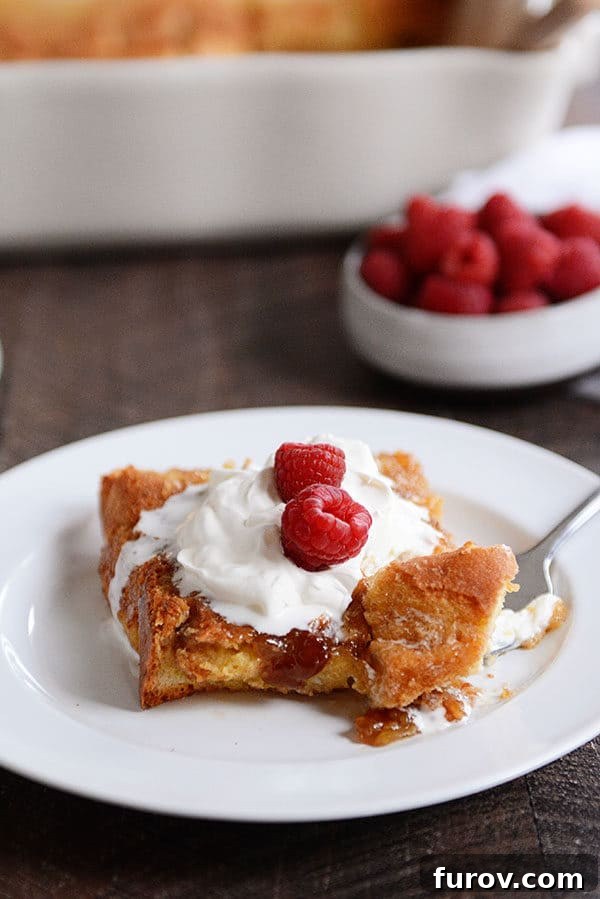 A fork taking a delicious bite out of a piece of creme brulee French toast, lavishly topped with whipped cream and fresh raspberries.