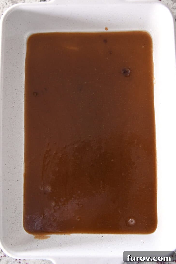 Top-down view of a ceramic white baking dish containing a melted cinnamon-butter-sugar mixture, forming the base of the French toast.
