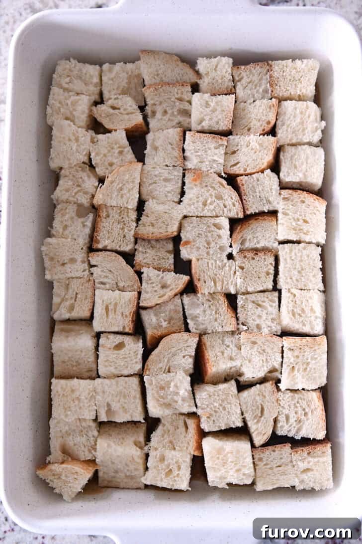 Top-down view of a white ceramic baking dish with thick, cubed pieces of French bread arranged in a single, even layer over the caramel mixture.