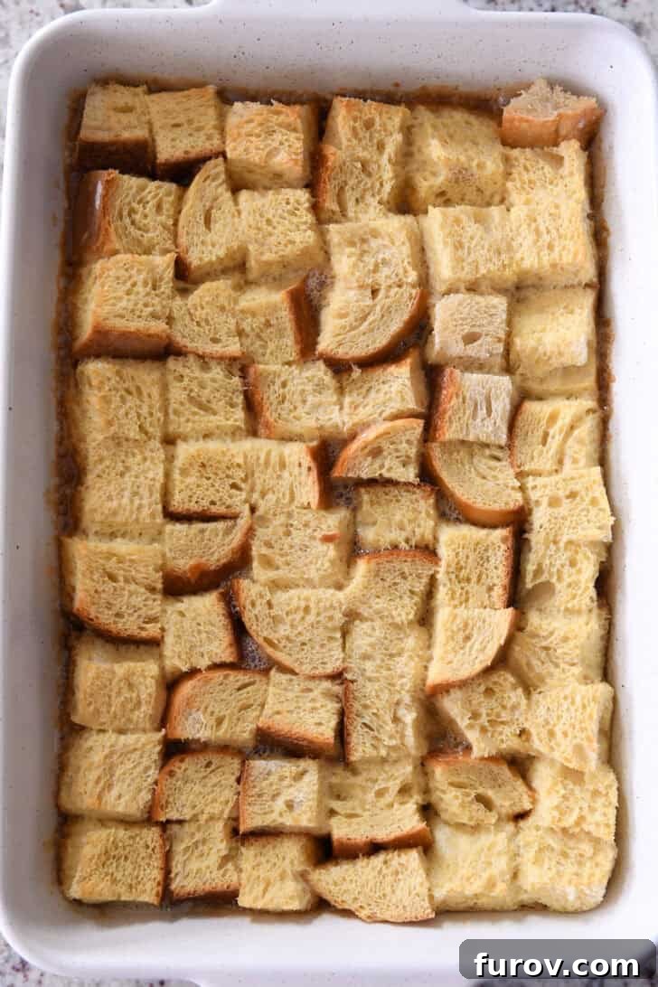 Top-down view of a white ceramic baking dish showing egg-coated bread chunks ready for refrigeration, after soaking in the custard mixture.
