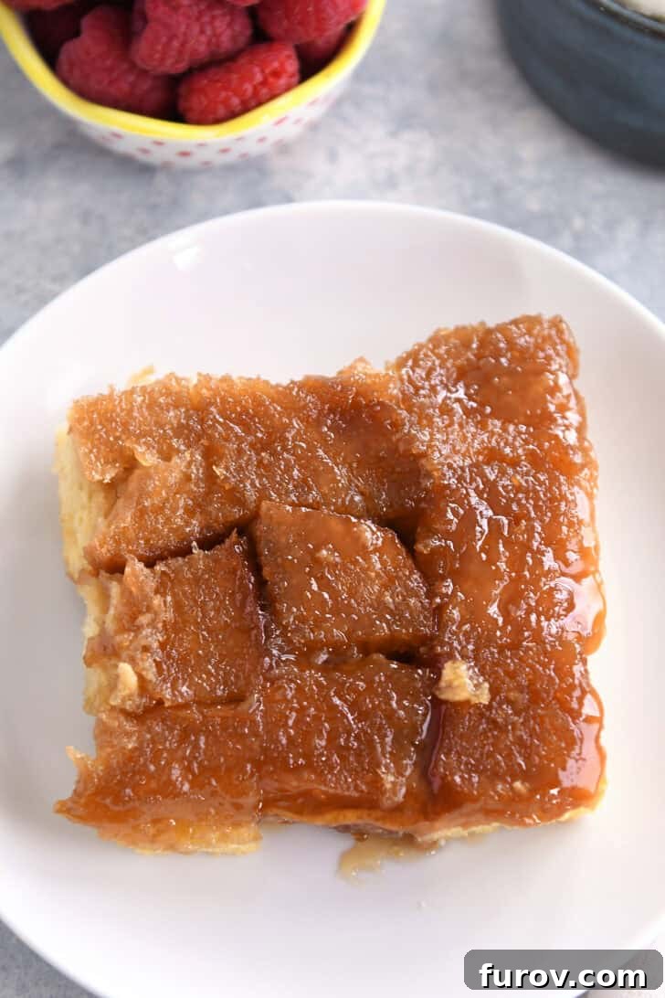 Close-up, top-down view of a single piece of sticky, caramelized creme brûlée French toast bake resting on a white plate, highlighting its golden crust.