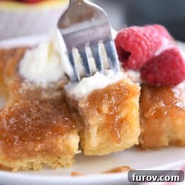A fork taking a bite out of a caramelized French toast bake on a white plate, highlighting the rich, golden texture.