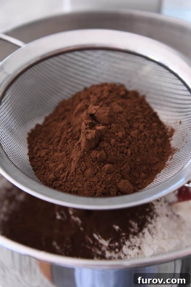 Pillowy Chocolate Frosted Swig Sugar Cookies 4 Close-up view of cocoa powder being carefully sifted into a bowl of light-colored cookie batter, highlighting the meticulous baking process.