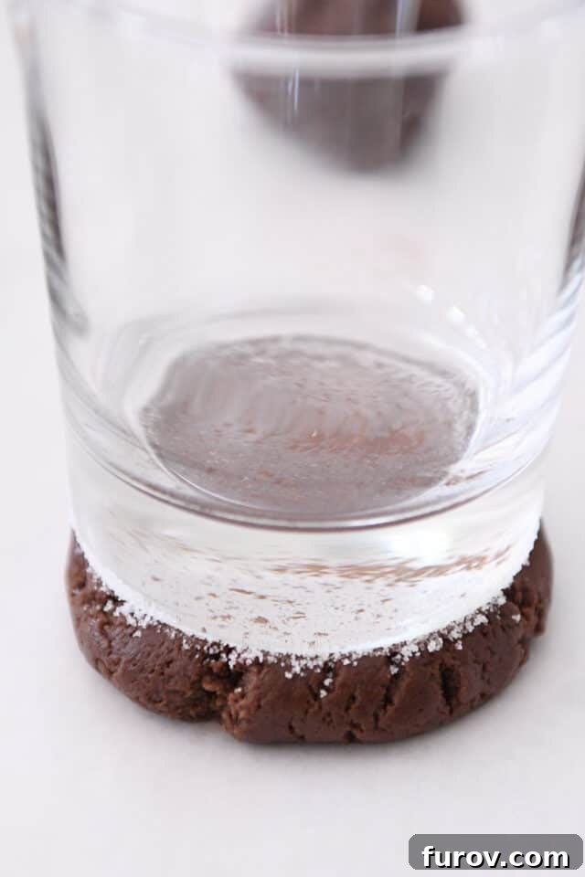 Pillowy Chocolate Frosted Swig Sugar Cookies 6 A baker gently presses a ball of chocolate cookie dough flat with a sugar-coated glass, demonstrating the signature Swig cookie shaping technique.