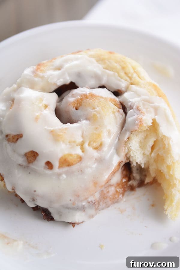 A frosted buttermilk biscuit cinnamon roll with a delicious bite taken out of it, showcasing the soft and buttery layers.