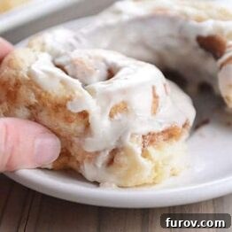 A hand pulling a bite off of a frosted cinnamon roll.